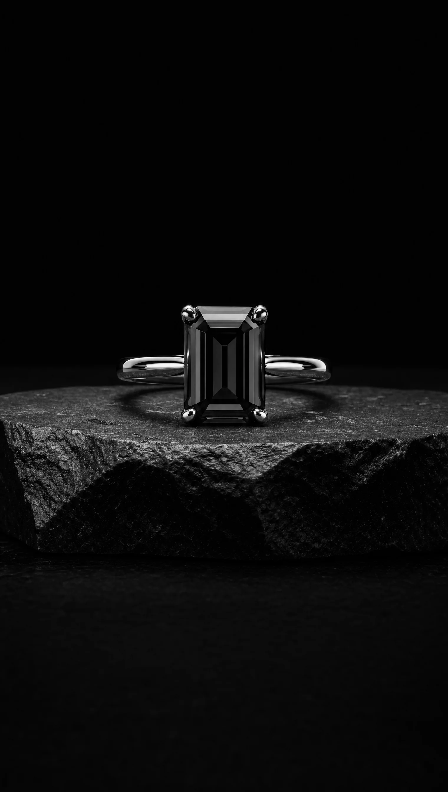 Black diamond emerald-cut solitaire ring in platinum on a black stone pedestal