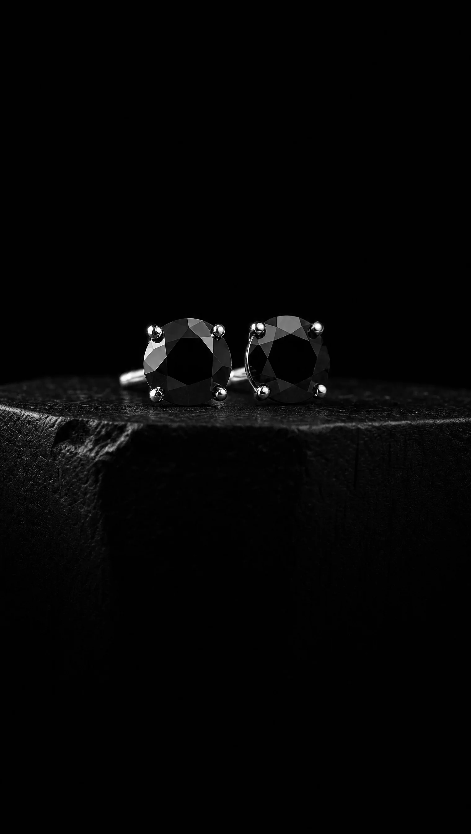 Pair of black diamond ear studs on a black stone pedestal