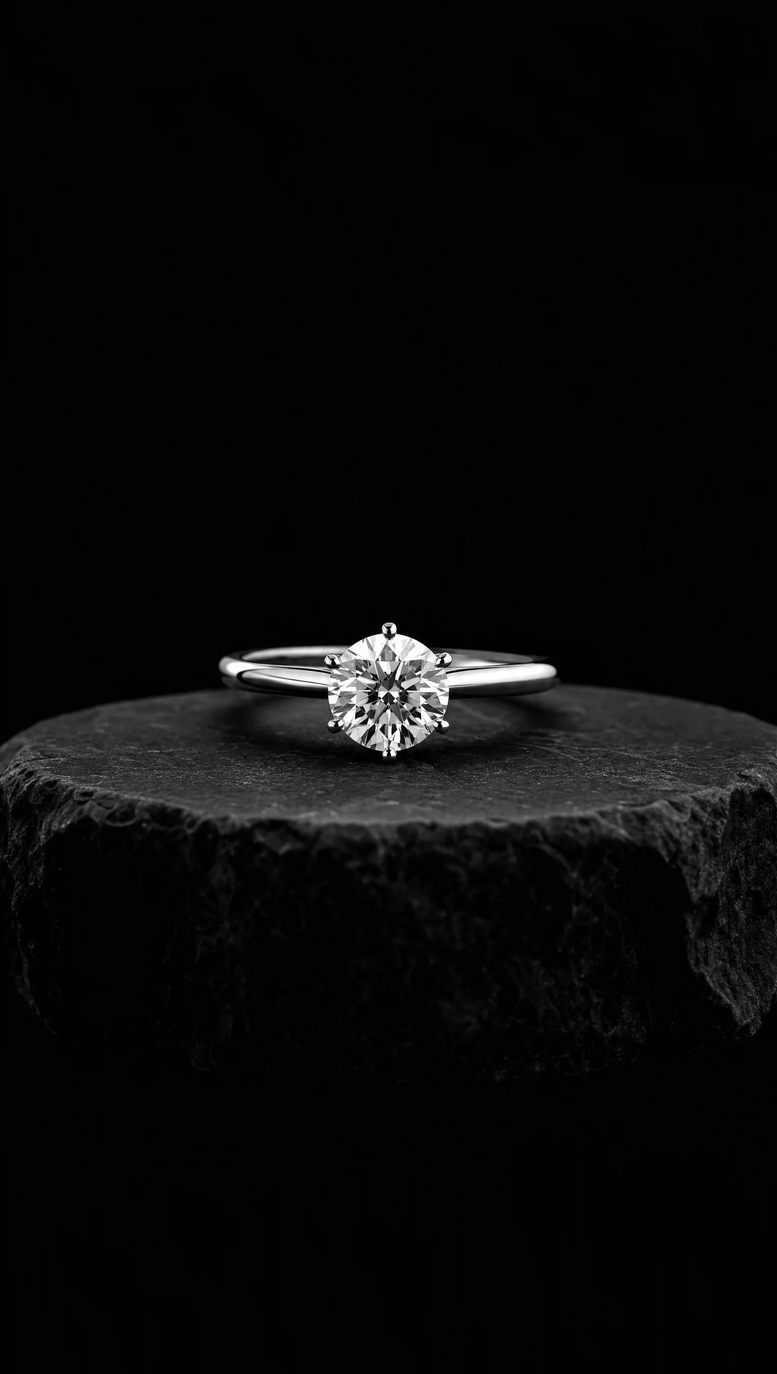 Round brilliant diamond solitaire ring on a thin platinum band, on a black stone pedestal