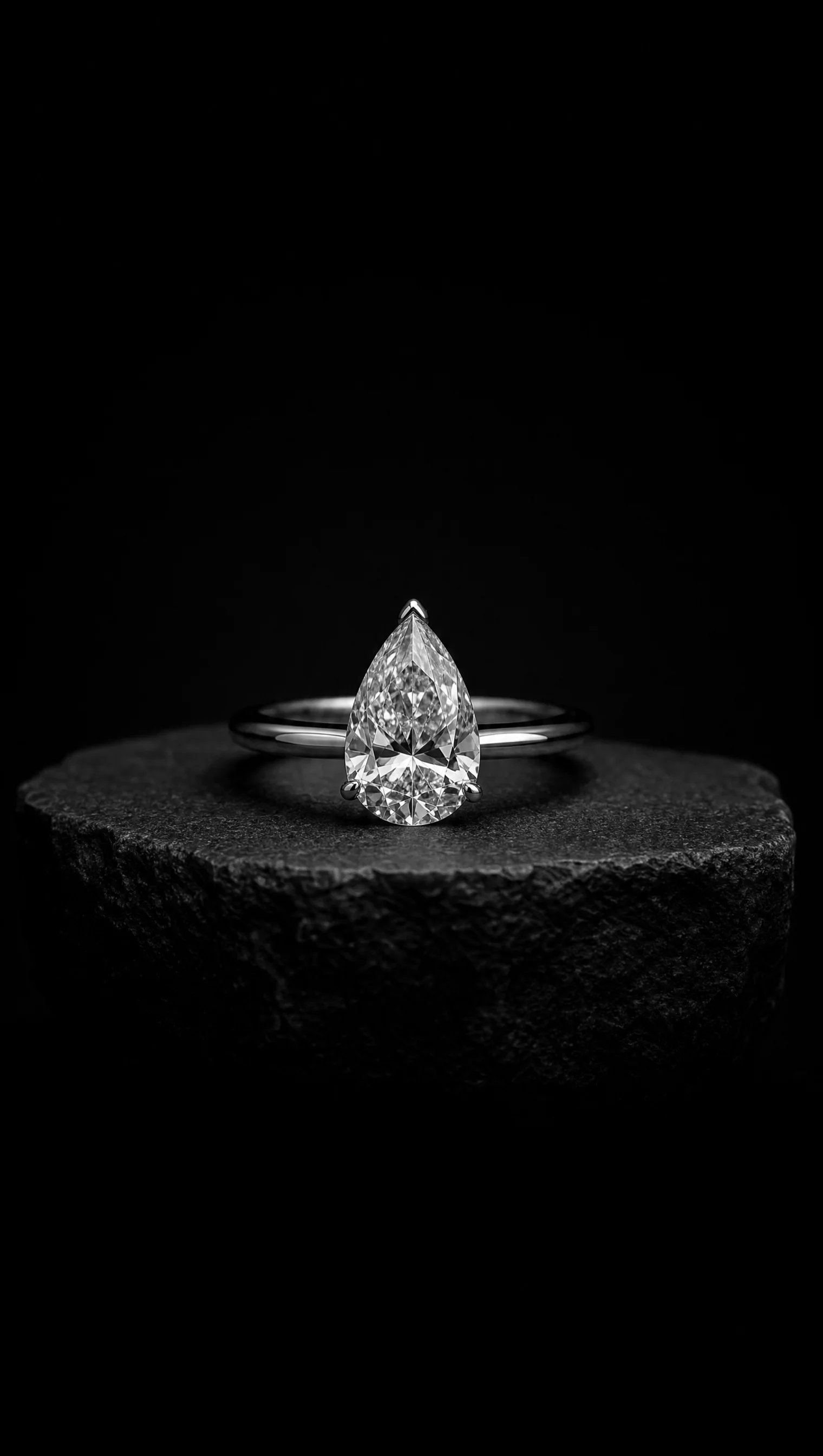 Pear-cut diamond solitaire ring in platinum on a black stone pedestal